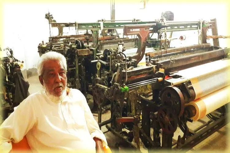 A weavers sits idle by the side of his power loom