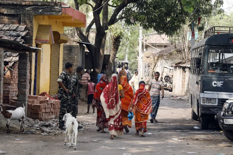 Paramilitary personnel stand guard as women of the violence-affected Beldona area under Samsergunj PS commute, in Murshidabad on Tuesday. 