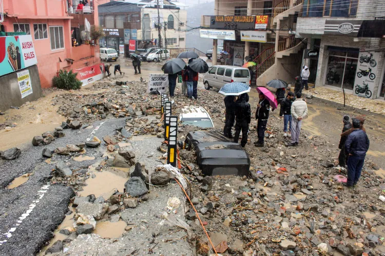 People look at the vehicles buried in sludge and debris following flash floods, in Kullu 
