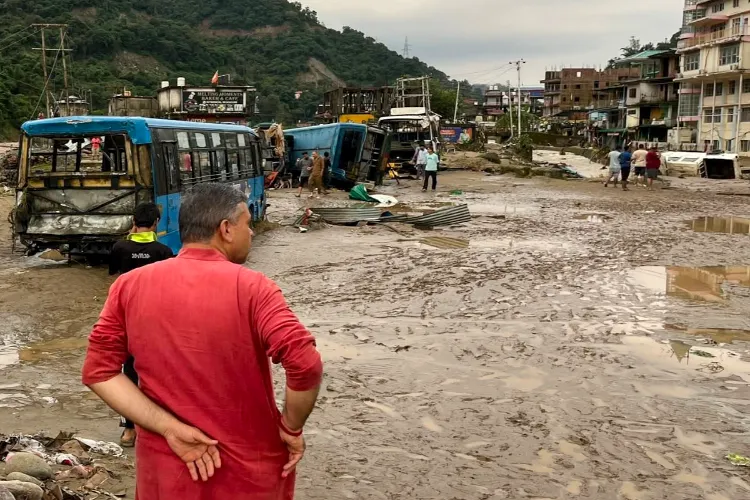 Mandi: People near the vehicles damaged due to floods triggered by heavy rains, at Dharampur in Mandi, Himachal Pradesh