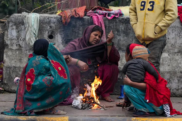 Women warm themselves near a small fire amid cold winter weather on a roadside, in New Delhi