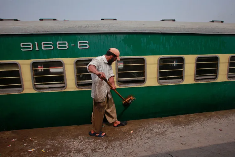 A man washes a passenger train carriage parked in a railway station yard in Lahore