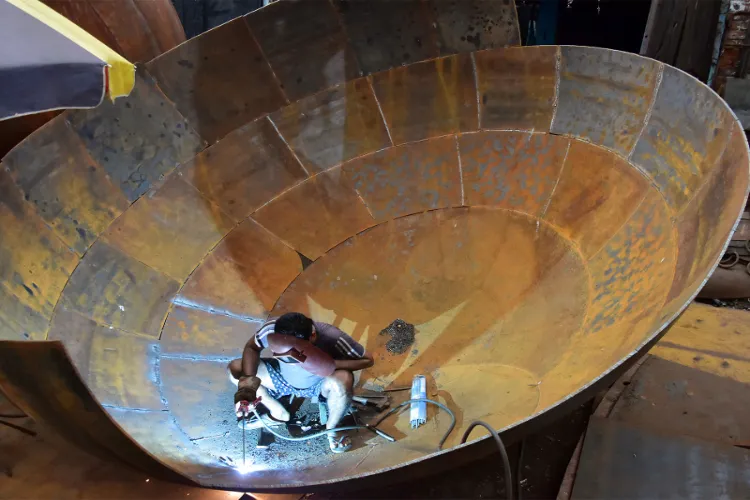 A labourer welding a giant iron pot at an iron factory in Kolkata
