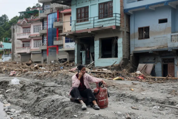A woman speaks on a phone as she sits next to a gas cylinder at the site of flash floods and mudslides, in Devighat