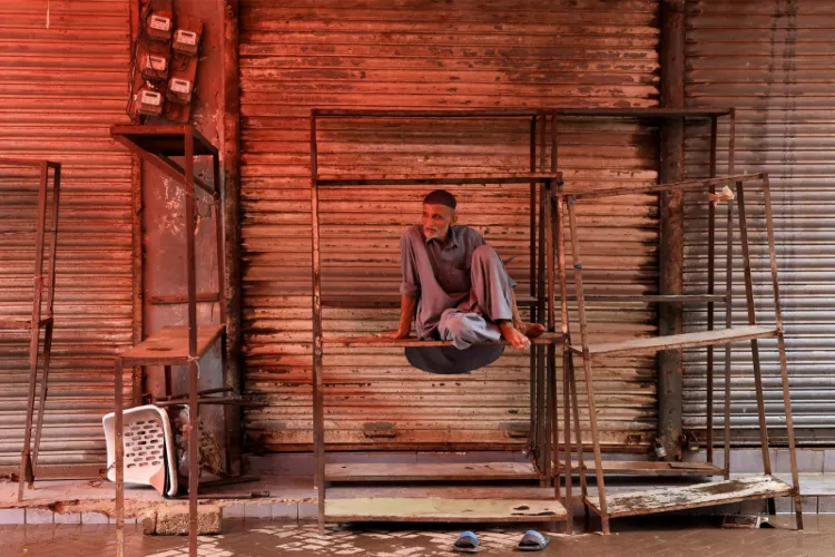 A salesman sits on iron frames outside closed shop in Pakistan