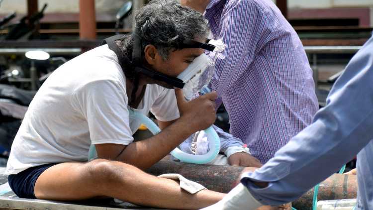 A COVID-19 patient sits on a stretcher, breathing with the support of an oxygen mask, outside the Swaroop Rani Nehru hospital in Prayagraj on Sunday