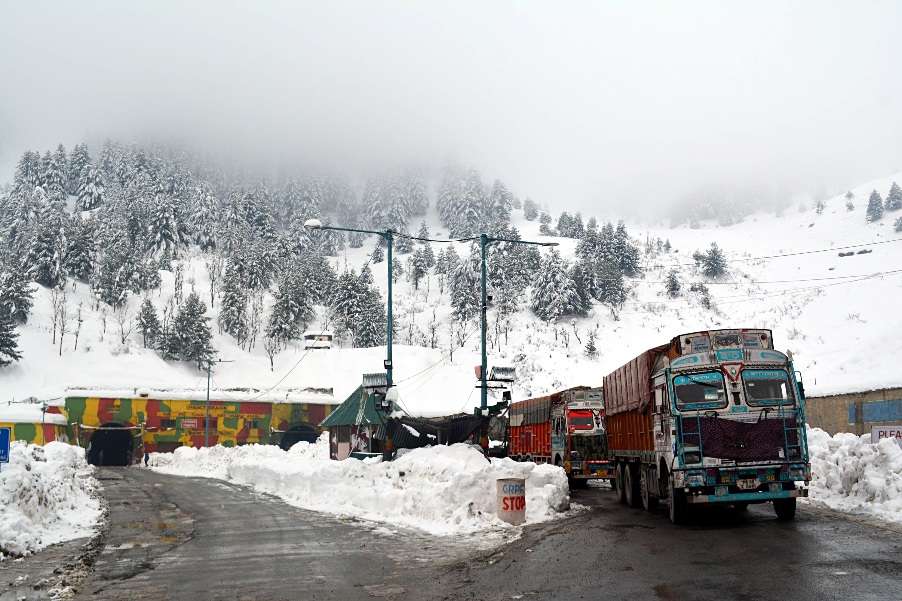 Trucks move on a snow-covered Srinagar-Jammu National Highway after snowfall at Qazigund, in Anantnag on Sunday.